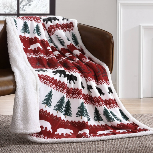 A cozy throw blanket with a red and white pattern featuring bears and trees, draped over a brown leather couch.