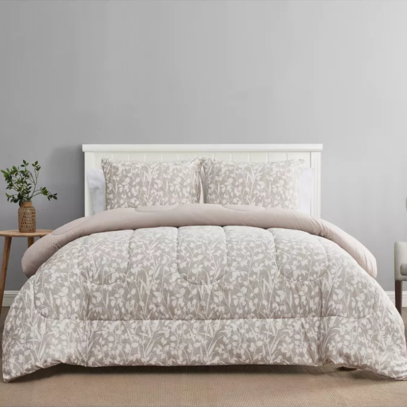 A bed with a floral-patterned comforter and matching pillows, set against a white headboard. A small table with a potted plant is on the left side.