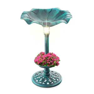 A teal, leaf-shaped solar lamp doubles as a planter, featuring pink flowers at its base and intricate decorative patterns on its round stand.