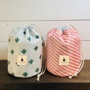 Two drawstring bags with different designs; one features green cacti on white, and the other has pink and white stripes.