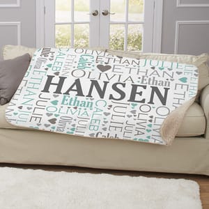 A personalized fleece blanket featuring the name \“Hansen\“ prominently, surrounded by smaller names \“Olivia,\“ \“Ethan,\“ \“Caleb,\“ and \“Julie,\“ with heart motifs in gray and teal on a sofa.