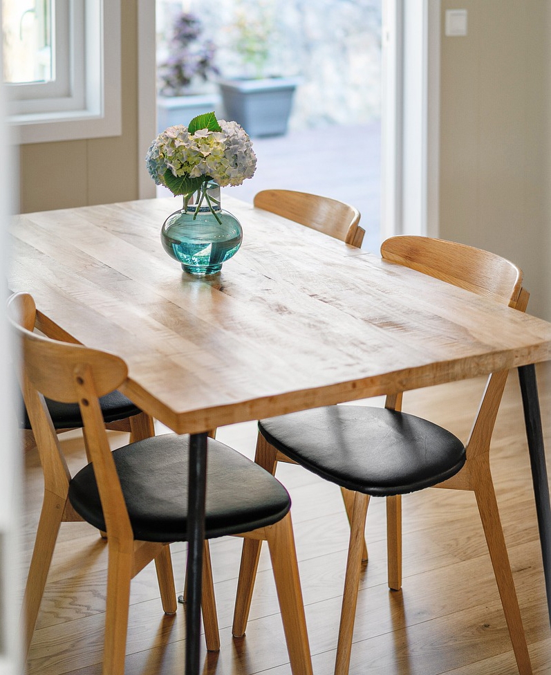 Wooden dining table with matching chairs and a glass vase holding hydrangeas.