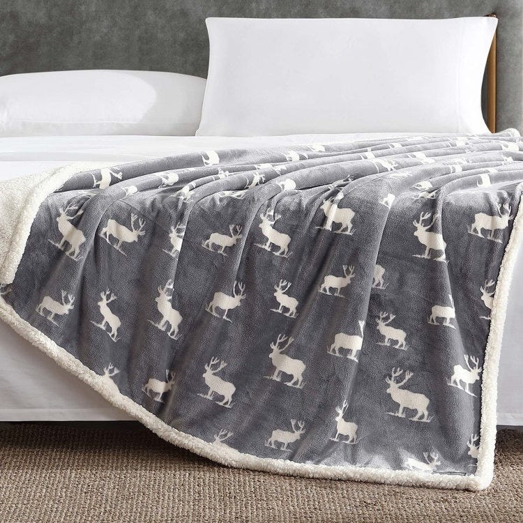 A gray fleece blanket with a white deer pattern is draped over a bed with white pillows.