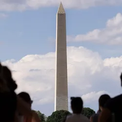 The photo shows the Washington Monument with people in silhouette in the foreground, set against a backdrop of cloudy skies.