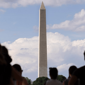The photo shows the Washington Monument with people in silhouette in the foreground, set against a backdrop of cloudy skies.