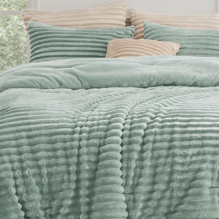 A plush, ribbed-texture teal comforter is shown with matching pillows and contrasting beige pillows, creating a cozy bedding set.