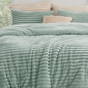 A plush, ribbed-texture teal comforter is shown with matching pillows and contrasting beige pillows, creating a cozy bedding set.