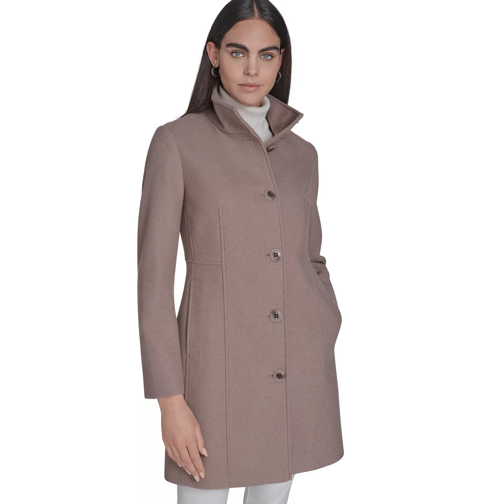 A woman is wearing a tailored, button-up taupe coat with a high collar over a white turtleneck, paired with white pants.