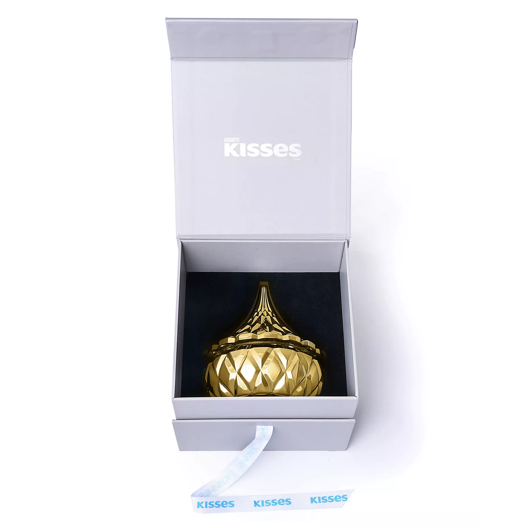 A decorative gold-colored container shaped like a Hershey's Kiss is displayed in an open white box with \“KISSES\“ printed on the inside lid.