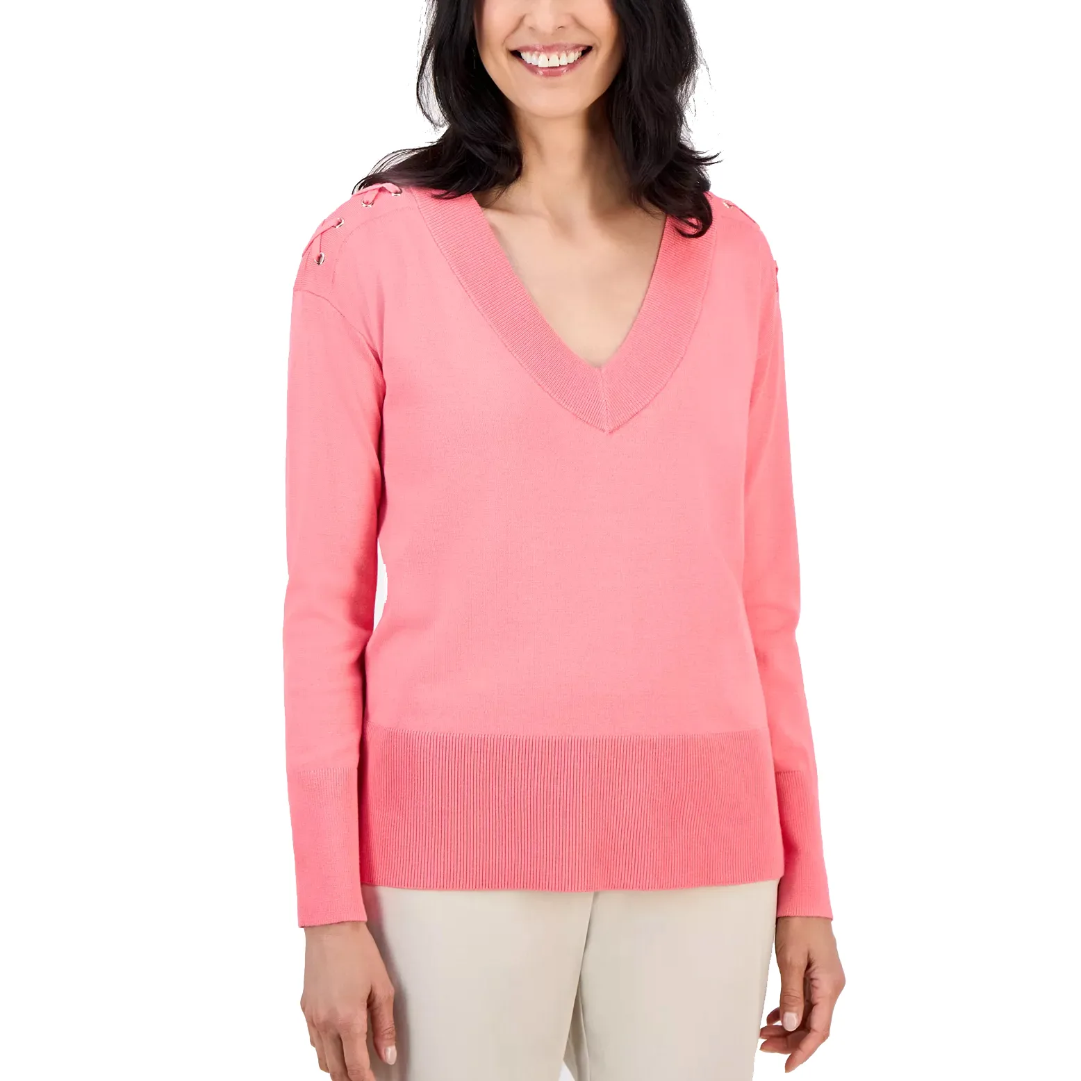 A woman is wearing a pink V-neck sweater with long sleeves and lace-up details on the shoulders, paired with light-colored pants.