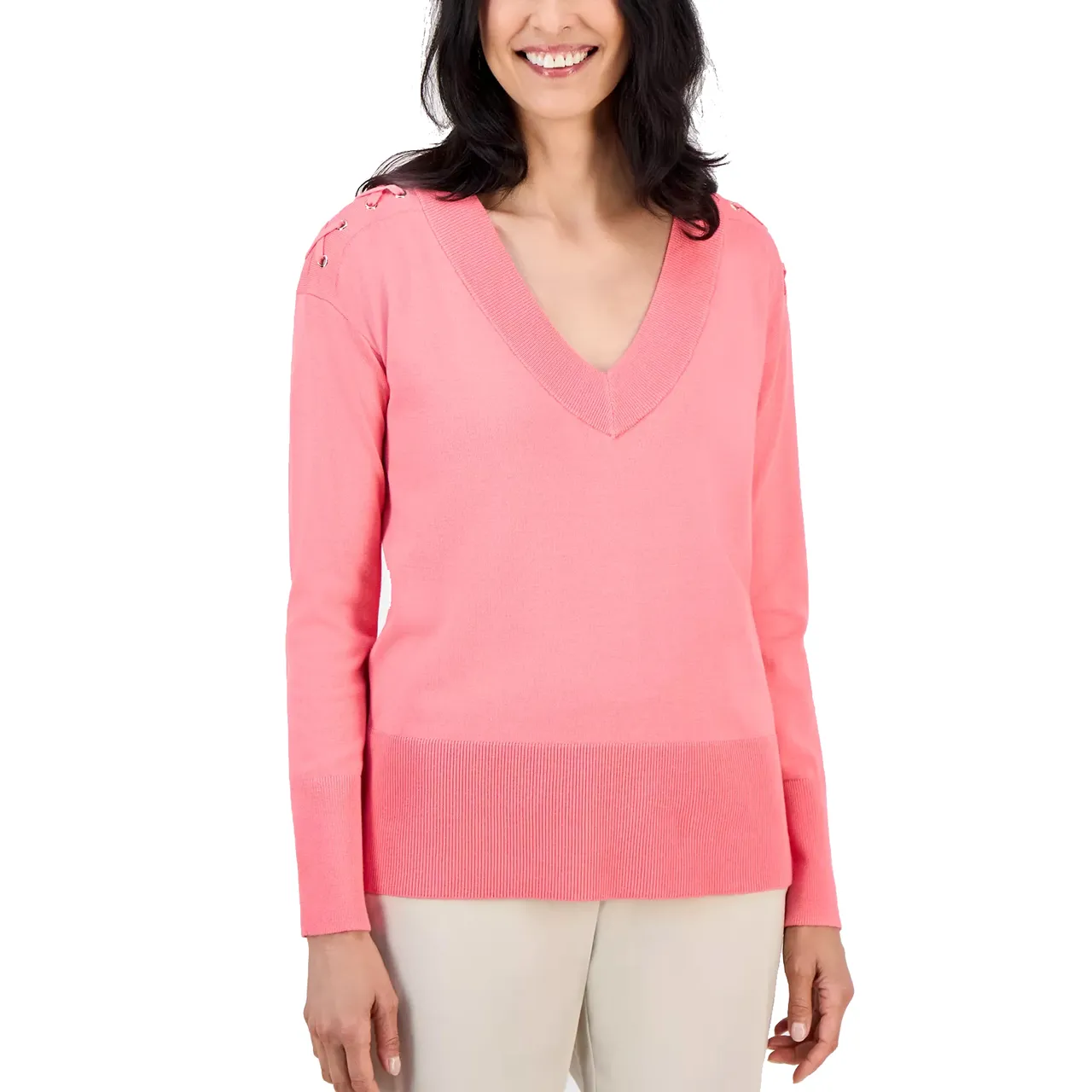 A woman is wearing a pink V-neck sweater with long sleeves and lace-up details on the shoulders, paired with light-colored pants.