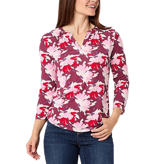 Woman wearing a floral-patterned, long-sleeve blouse in pink, purple, and red tones with a V-neckline, paired with blue jeans.