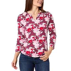 Woman wearing a floral-patterned, long-sleeve blouse in pink, purple, and red tones with a V-neckline, paired with blue jeans.