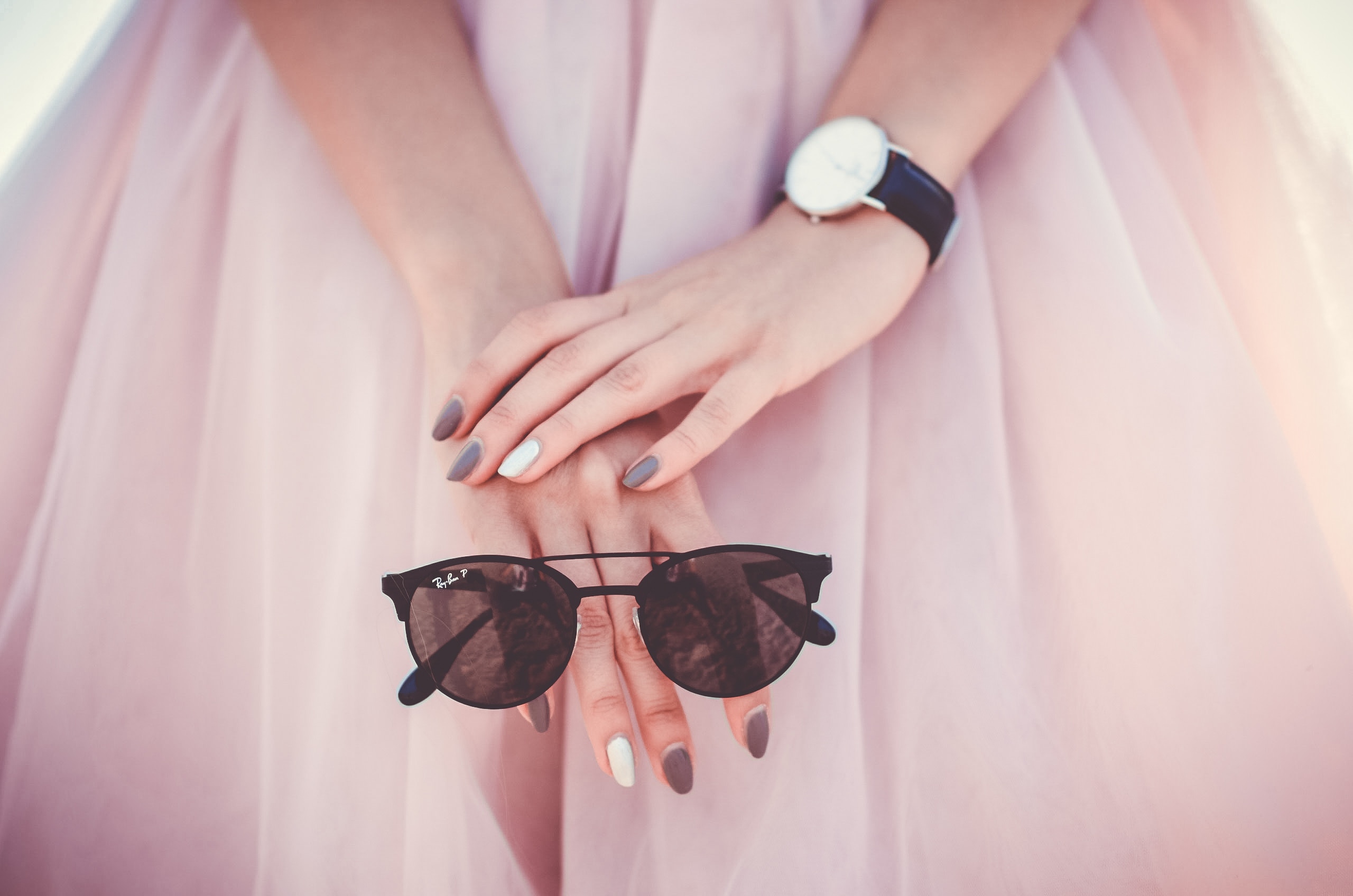 A person is holding a pair of sunglasses and wearing a wristwatch.