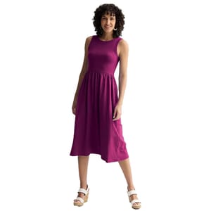 A woman is wearing a sleeveless, knee-length, magenta dress paired with white wedge sandals.
