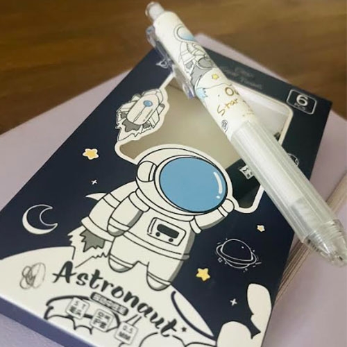 A white pen with space-themed designs and a matching notebook featuring an astronaut illustration.