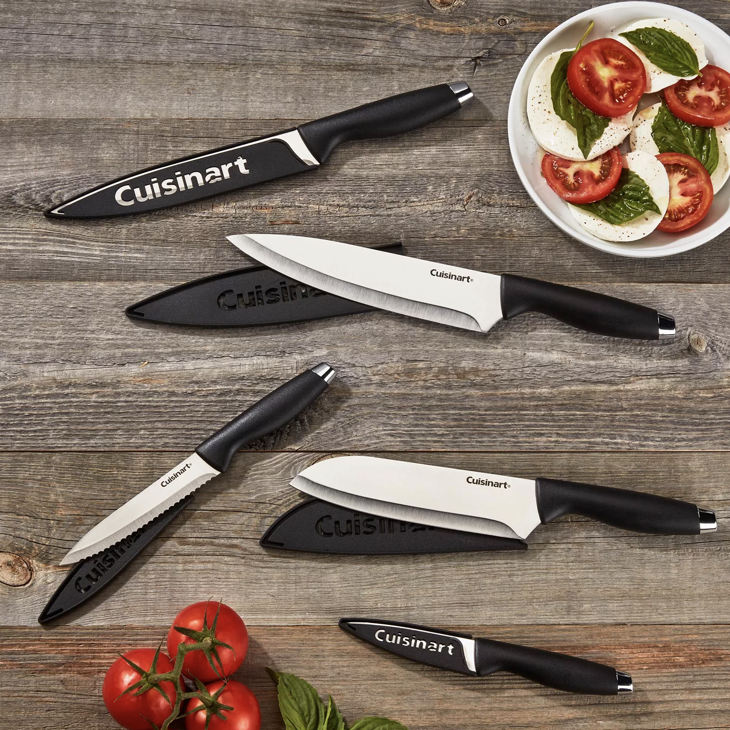Set of Cuisinart knives with black handles and protective sleeves displayed on a wooden surface, accompanied by sliced mozzarella and tomato basil salad.