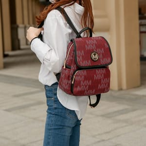 A person is wearing a white blouse and blue jeans, carrying a burgundy backpack with a repeating logo pattern.