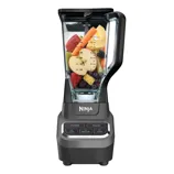 A Ninja blender featuring a transparent container filled with assorted fruits and vegetables, including strawberries, apples, pineapples, and blueberries. The blender has power, pulse, and speed settings (low, medium, high).