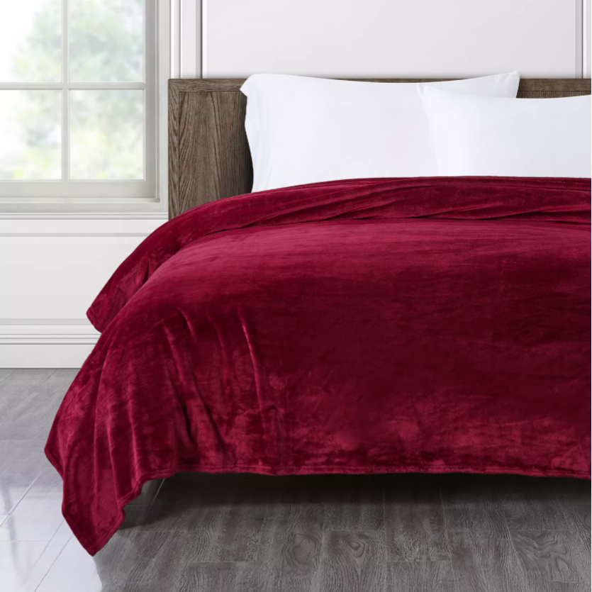 A red velvet blanket is draped over a bed, with white pillows and a wooden headboard.