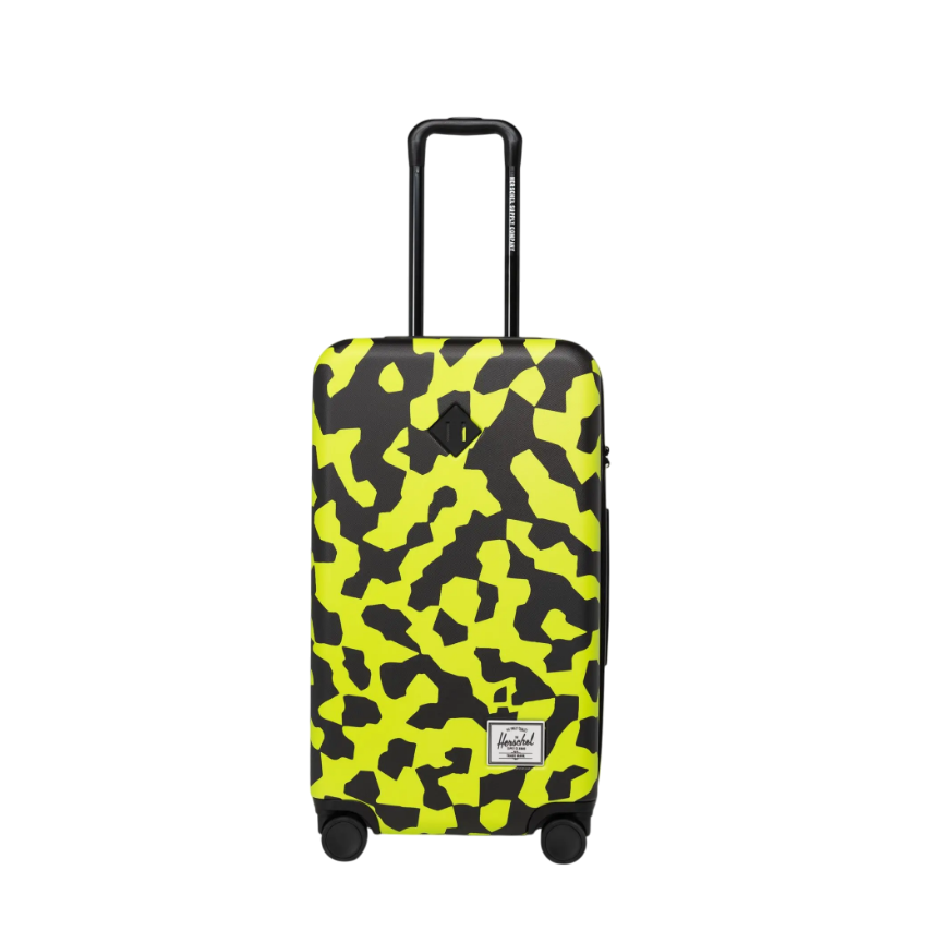 Yellow and black abstract-patterned hard-shell suitcase with a retractable handle and four wheels, featuring a small patch on the front.