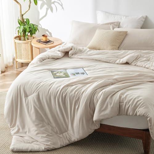 A cozy beige bed set with a comforter, pillows, and a magazine lies next to a small wooden table with a plant, all in a sunlit room.