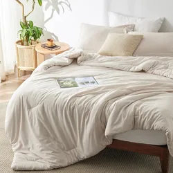 A cozy beige bed set with a comforter, pillows, and a magazine lies next to a small wooden table with a plant, all in a sunlit room.
