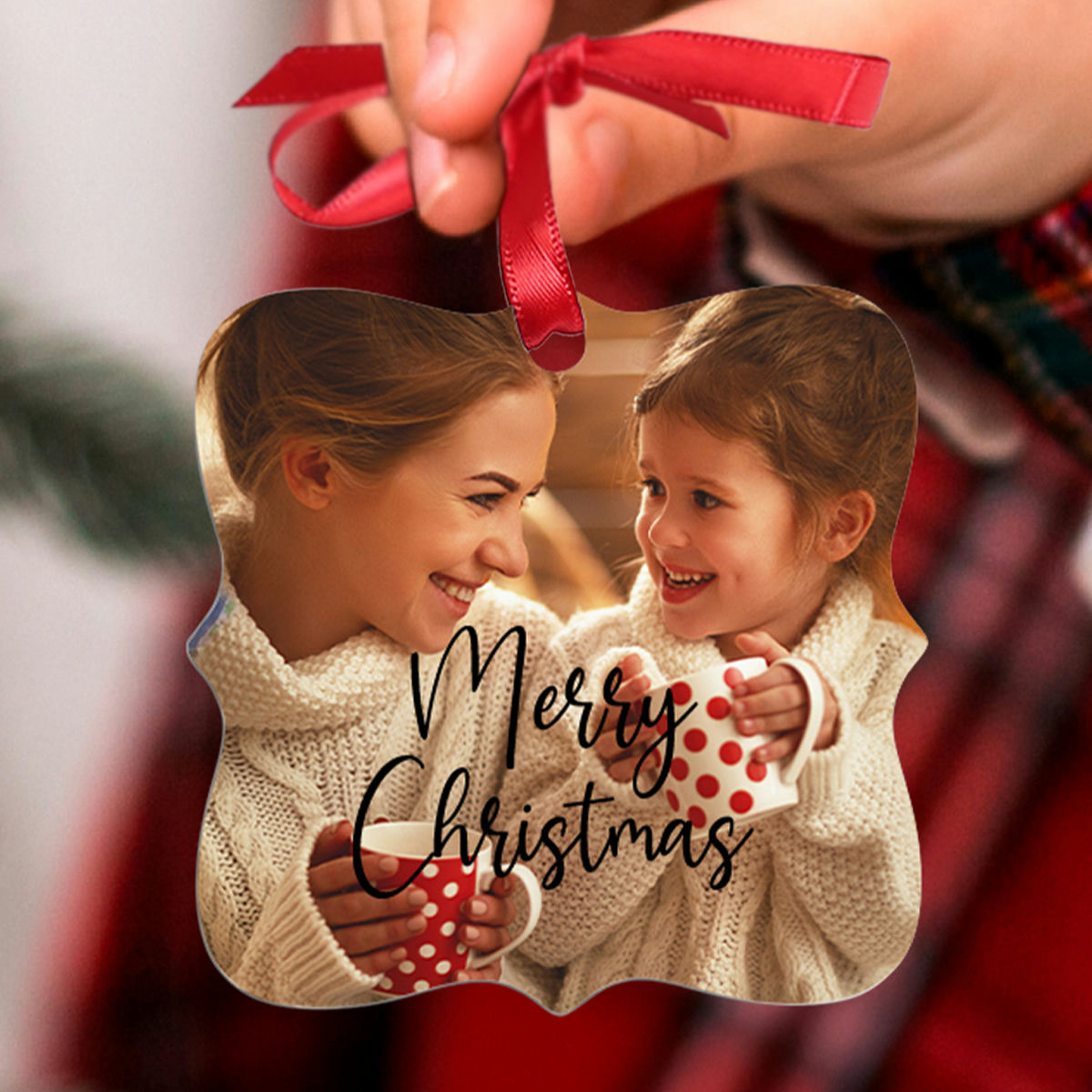 A Christmas ornament features two people in cozy sweaters, smiling and holding red polka dot mugs, with \“Merry Christmas\“ written on it.