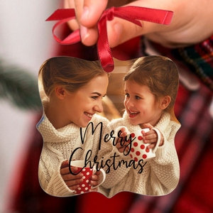 A Christmas ornament features two people in cozy sweaters, smiling and holding red polka dot mugs, with \“Merry Christmas\“ written on it.