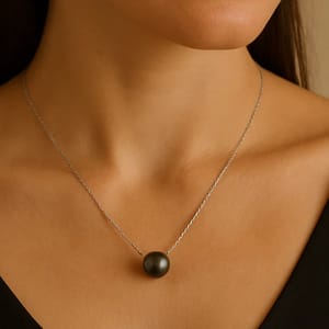 A woman is wearing a silver chain necklace with a single large black pearl pendant, set against a black top.