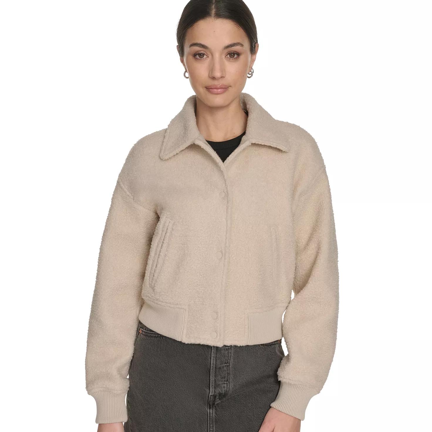 A woman is wearing a light beige shearling jacket with a collar, ribbed cuffs, and a button front, paired with dark high-waisted jeans.
