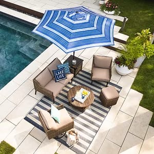A blue and white striped patio umbrella providing shade to an outdoor seating area with two chairs, a sofa, and a coffee table.