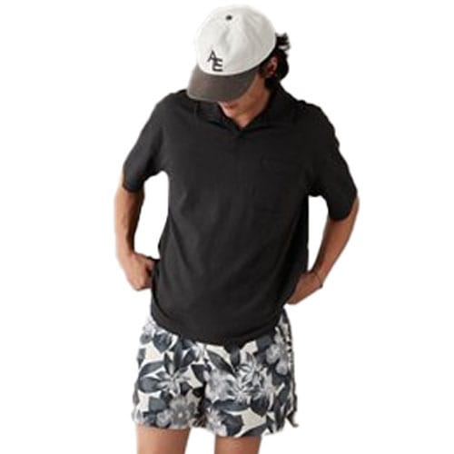 A man is wearing a black short-sleeved polo shirt with a collar and a button-up placket, paired with patterned shorts.