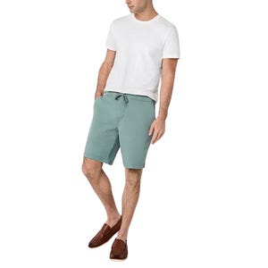 Comfortable 9\“ canvas shorts in a muted teal color, featuring an elastic waistband with a drawstring for adjustability, paired with a white t-shirt and brown loafers.