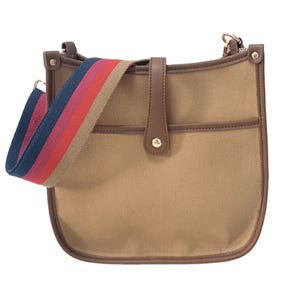 Brown canvas courier bag with leather trim and a colorful adjustable strap featuring tan, red, and blue stripes. It has a front pocket and a simple button closure.