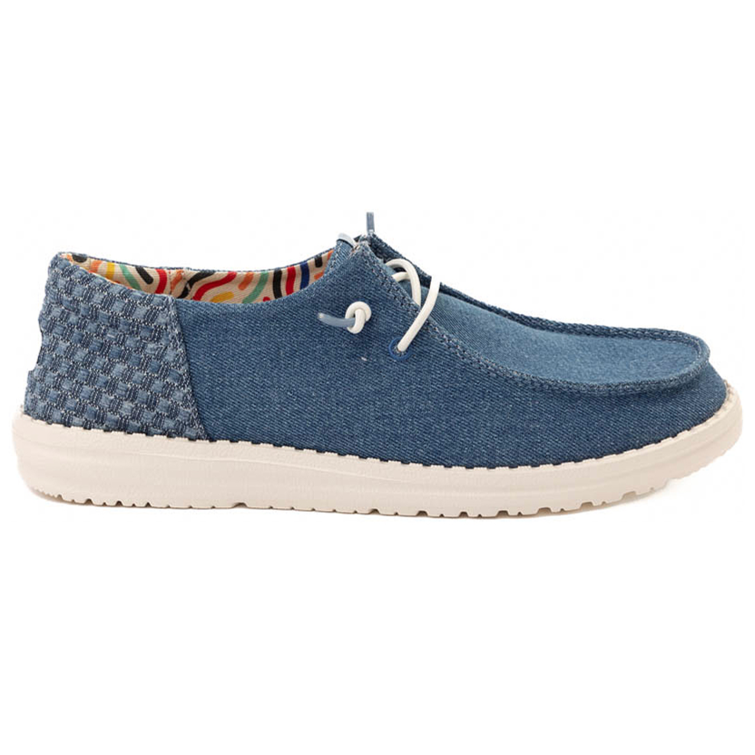 A casual denim slip-on shoe with white laces, featuring a textured heel and a multicolored interior lining, set on a white rubber sole.