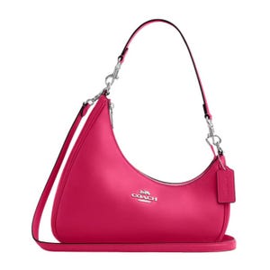 A bright pink Coach shoulder bag with a curved design, detachable strap, and silver hardware. The logo is prominently displayed on the front.