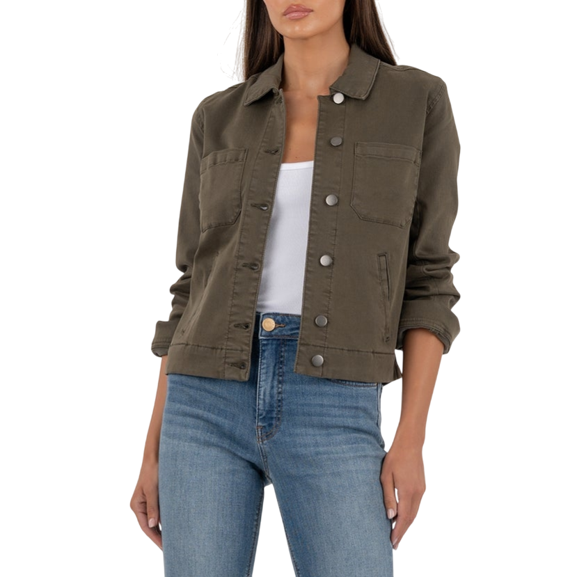 A woman is wearing a khaki button-up jacket, white tank top, blue high-waisted flared jeans, and black-and-white sneakers.