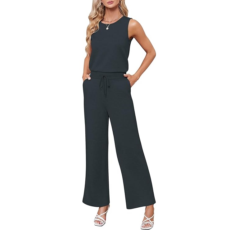 A woman is wearing a sleeveless black jumpsuit with wide-leg pants and a drawstring waist, paired with white strappy heels.