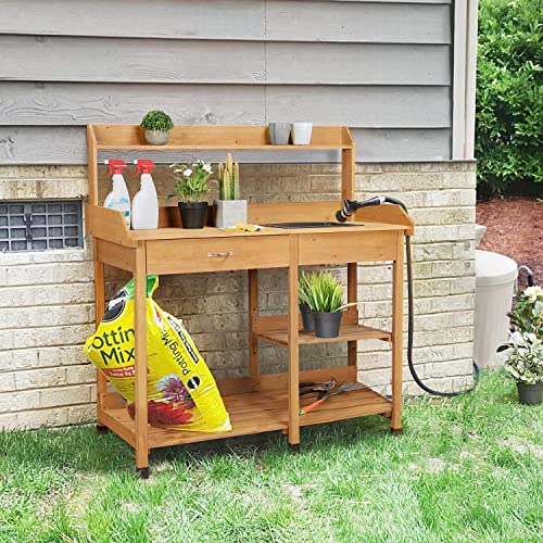 A wooden potting bench with shelves, a worktop space, and a slatted back for hanging tools, positioned against a house with various gardening supplies on and around it.