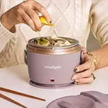 Person using a Crockpot lunch warmer, adding a lemon wedge for flavor to a dish, with chopsticks nearby.
