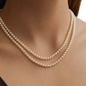 A double-strand necklace with round, white pearls draped around a woman's neck, against her skin and a dark-colored top.