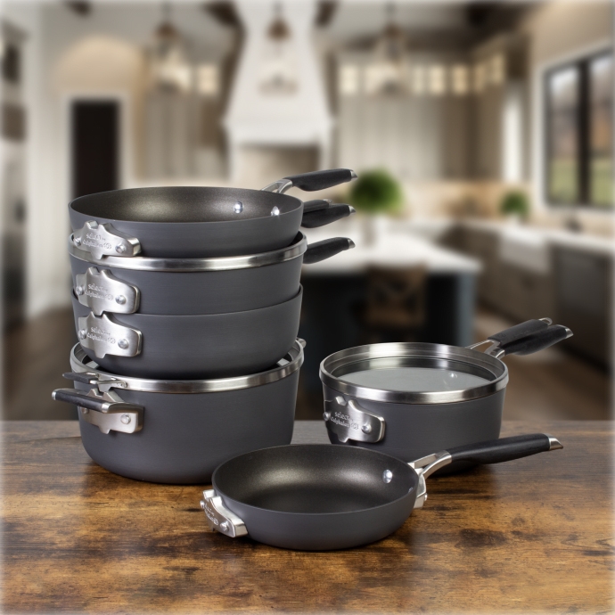 A set of gray non-stick pans and pots with black handles on a wooden surface, kitchen background.