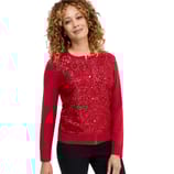 A woman is wearing a red cardigan adorned with sequins, featuring a button-up front. Her curly hair frames her face, and she is paired with black pants.
