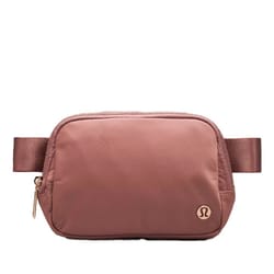 A small, brown belt bag with a simple design and metal zipper hardware, featuring a logo in the bottom right corner.