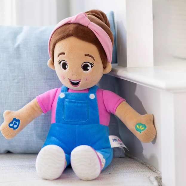 A plush doll with brown hair, wearing a pink headband, blue overalls, and a pink shirt.