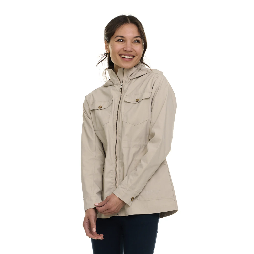 A woman is wearing a light beige jacket with a zip-up front and buttoned chest pockets. The jacket has a hood and is paired with dark jeans.