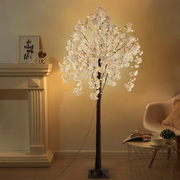 A decorative artificial cherry tree with illuminated blossoms provides ambient lighting in a cozy room setting.