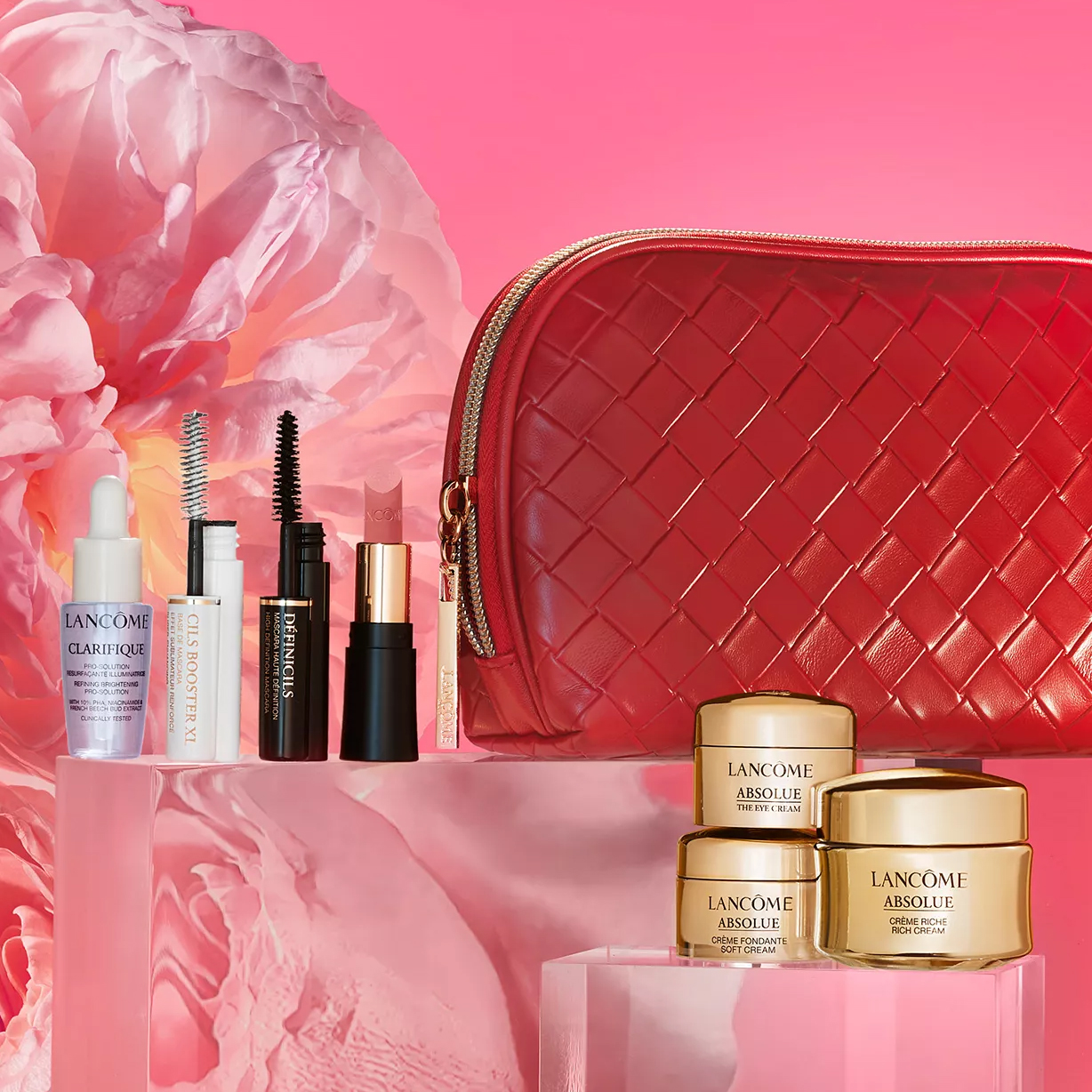 Lancôme beauty set featuring skincare items, mascara, lipstick, and a red textured cosmetic bag, displayed on a pink floral background.