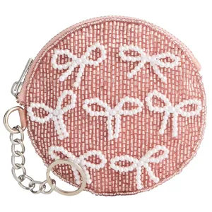 Round pink coin purse adorned with white beads shaped like bows, featuring a zipper closure and a metal keychain attachment.